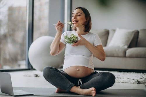 joven embarazada comiendo ensalada casa